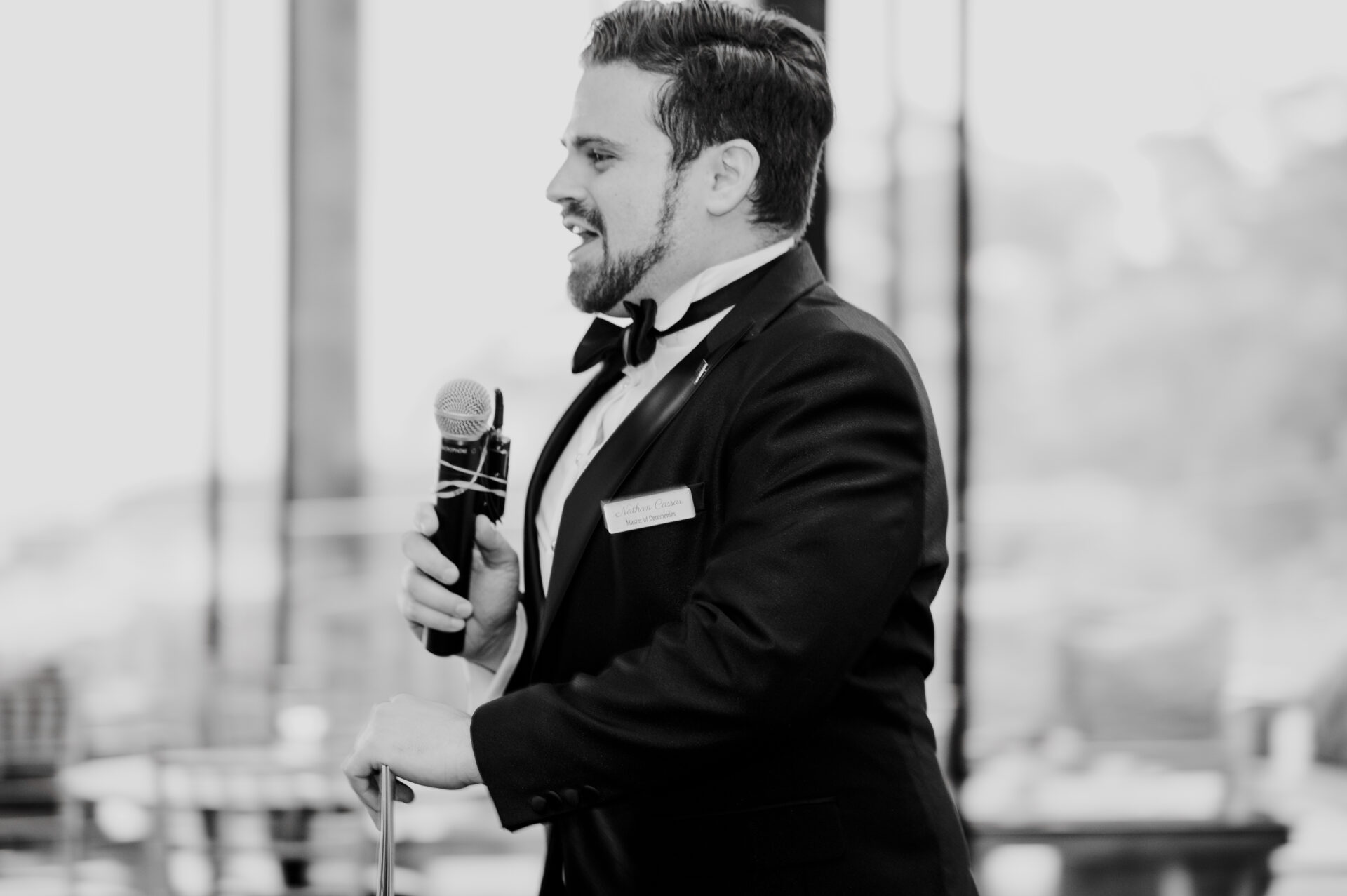 Nathan Cassar side profile black and white, talking into a microphone in a tuxedo