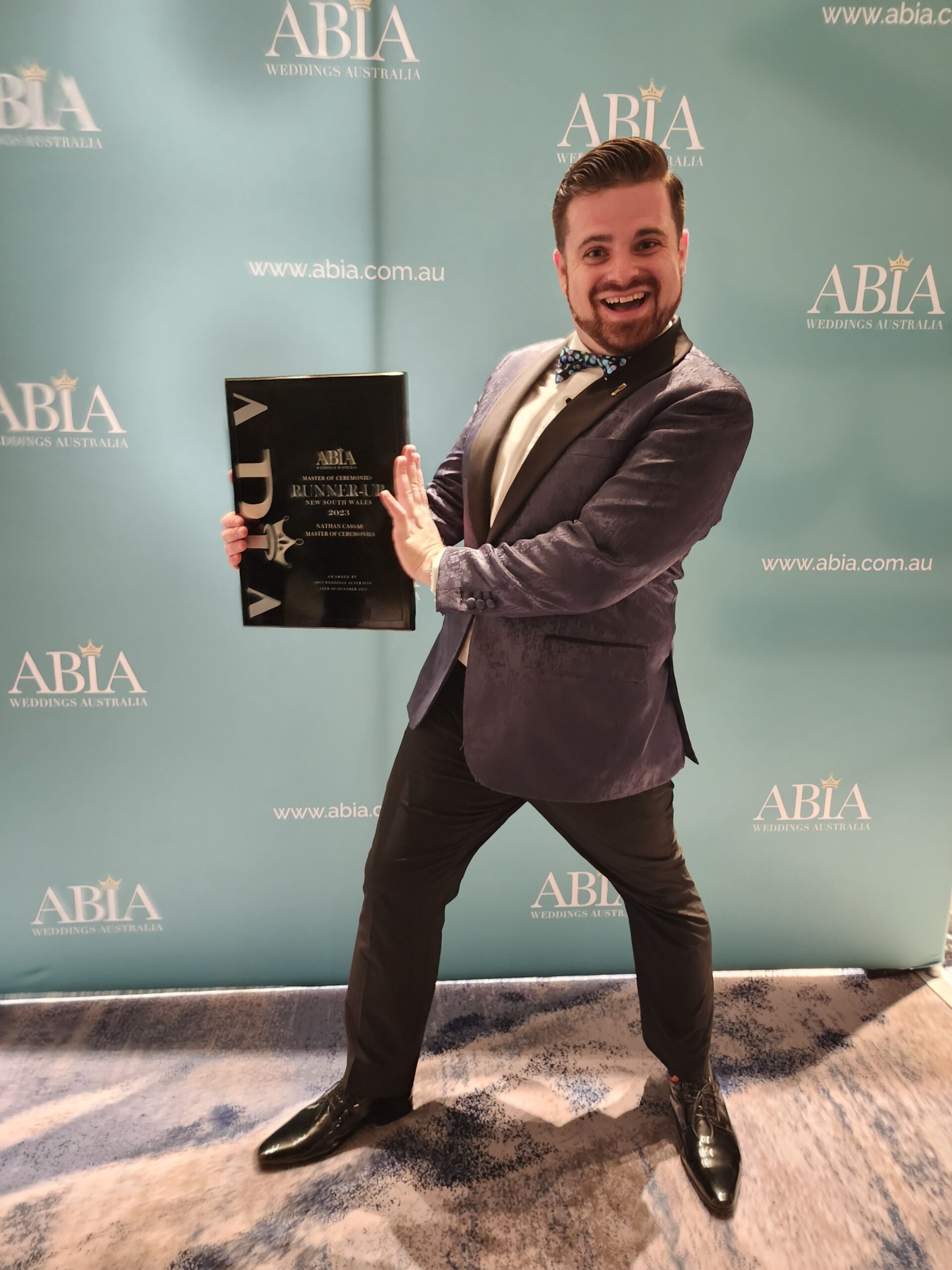 Nathan Cassar Master of Ceremonies in a blue tuxedo holding the Runner Up award in the 2023 ABIA Wedding Awards for Best MC (NSW)