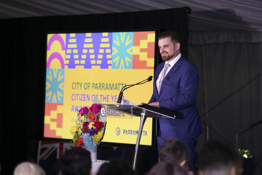 Nathan Cassar Master of Ceremonies hosting from a lectern the City of Parramatta 2024 Citizen of the Year presentation in a blue suit