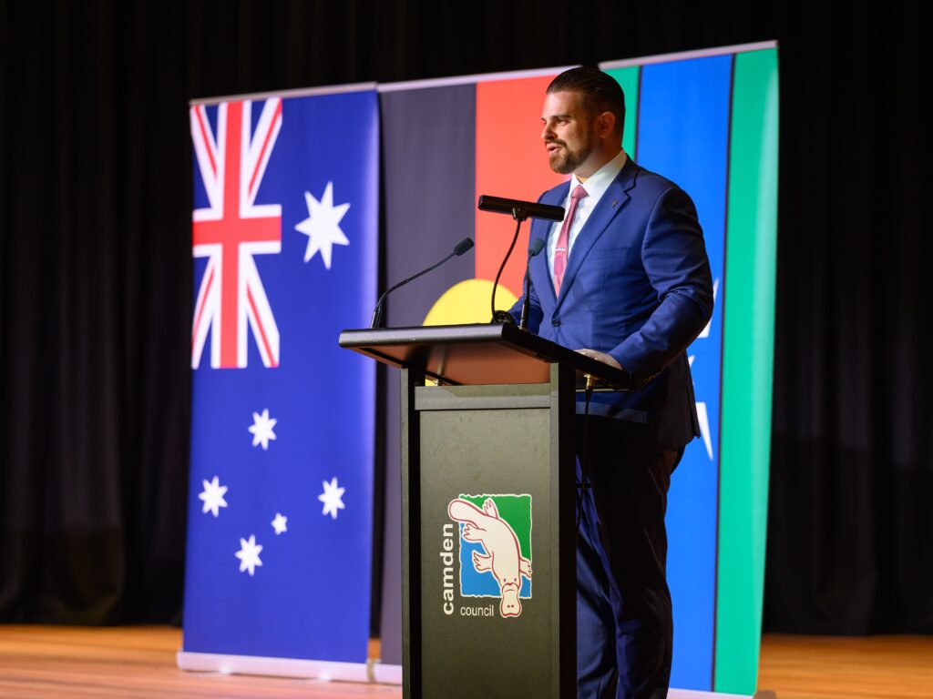 Nathan Cassar, corporate event mc speaking at Camden Council event with flags