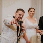 Groom giving speech, pointing, beside bride at reception