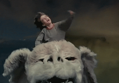 Boy raising his hand while flying on top of a dragon head in the sky