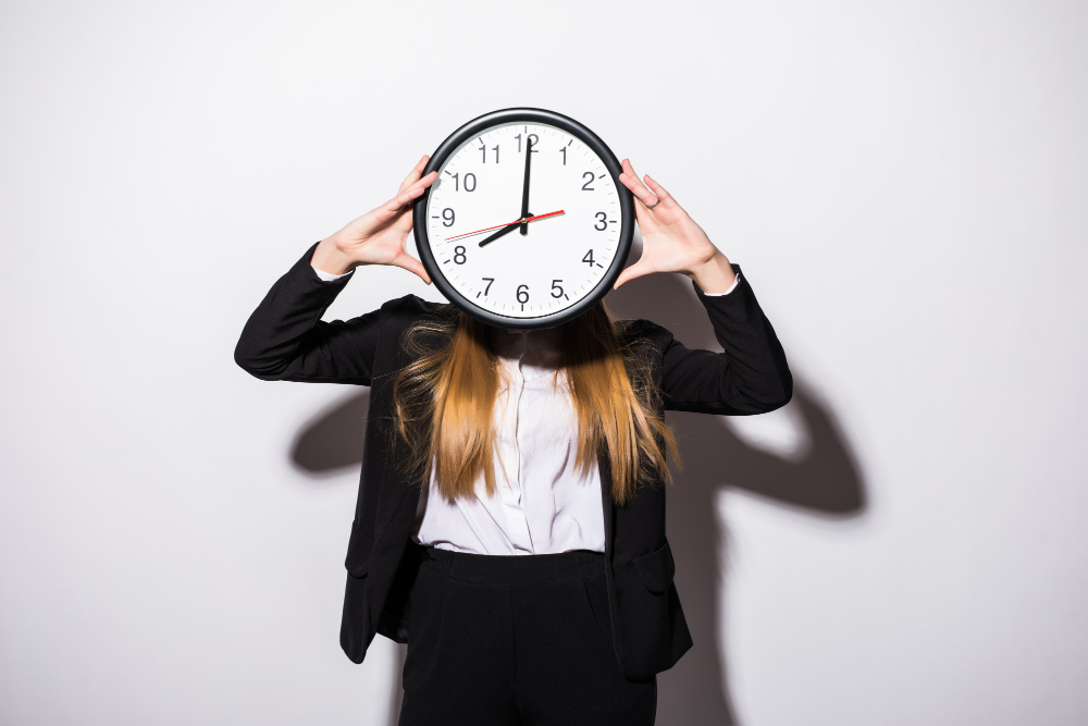 young business woman holding clock in front of face on white